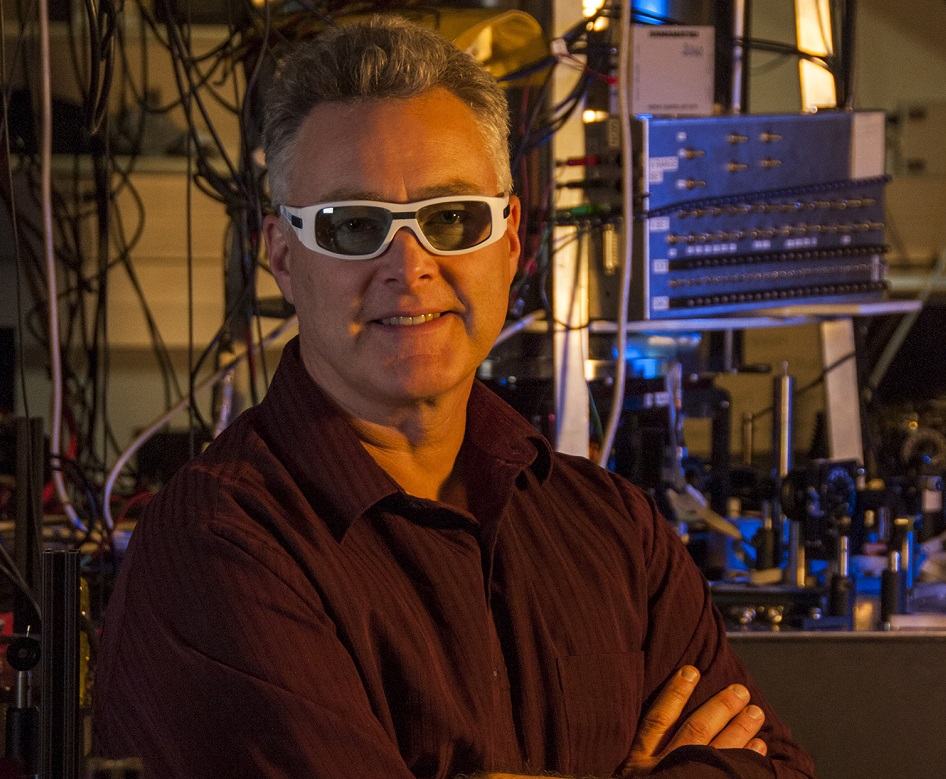 NIST researchers have demonstrated fine control of two ions confined in separate zones of an electric-field trap, which is chilled to low temperatures in the silver chamber behind Wilson. The techniques will be useful in simulating complex quantum systems such as high-temperature superconductors.  Credit: James Burrus/NIST